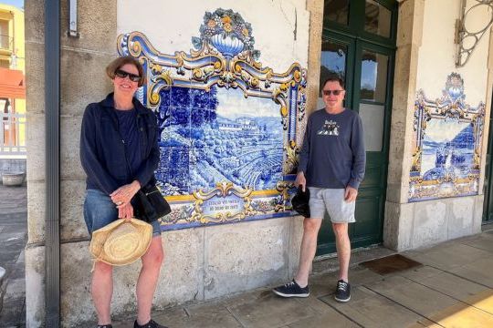 Two people stand before a building adorned with blue and white tiles during a private tour of the Douro Valley train station.