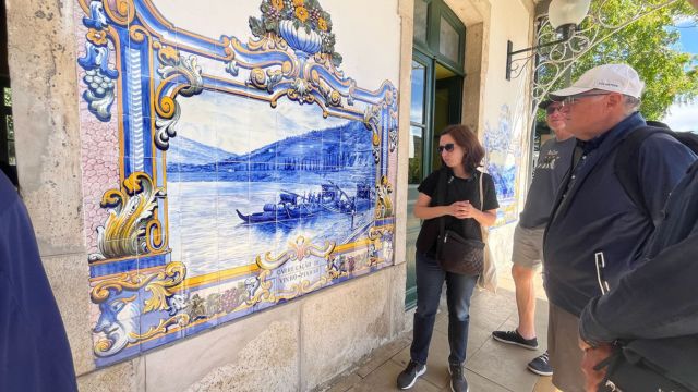 the tour guide in front of a blue and white tiled building, enjoying a private tour inside the Douro Valley train station.