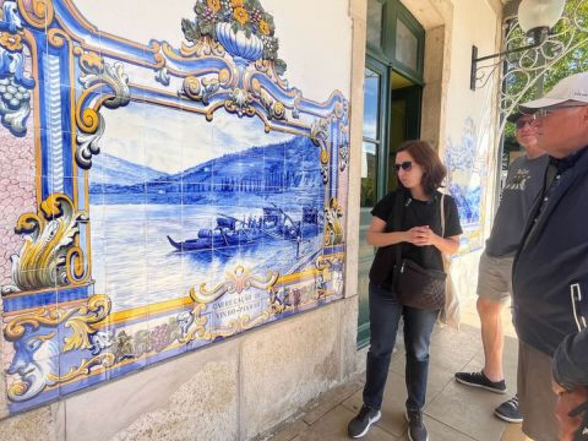 the tour guide in front of a blue and white tiled building, enjoying a private tour inside the Douro Valley train station.