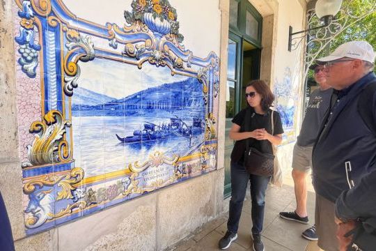 the tour guide in front of a blue and white tiled building, enjoying a private tour inside the Douro Valley train station.