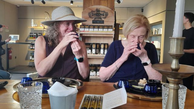 Two women at a table in Porto, hands on their mouths, enjoying the aroma of olive oil.