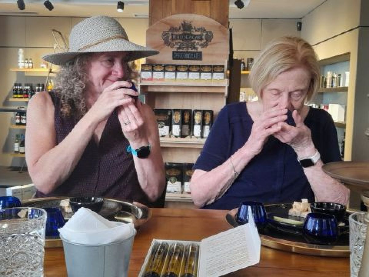 Two women at a table in Porto, hands on their mouths, enjoying the aroma of olive oil.