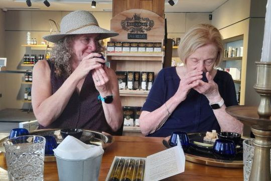 Two women at a table in Porto, hands on their mouths, enjoying the aroma of olive oil.