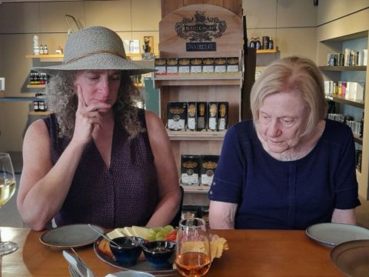 Two women enjoying wine at a table, surrounded by olive oil and food during a tasting event in Porto.
