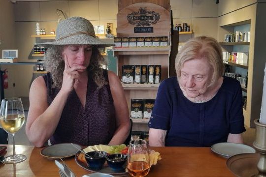 Two women enjoying wine at a table, surrounded by olive oil and food during a tasting event in Porto.