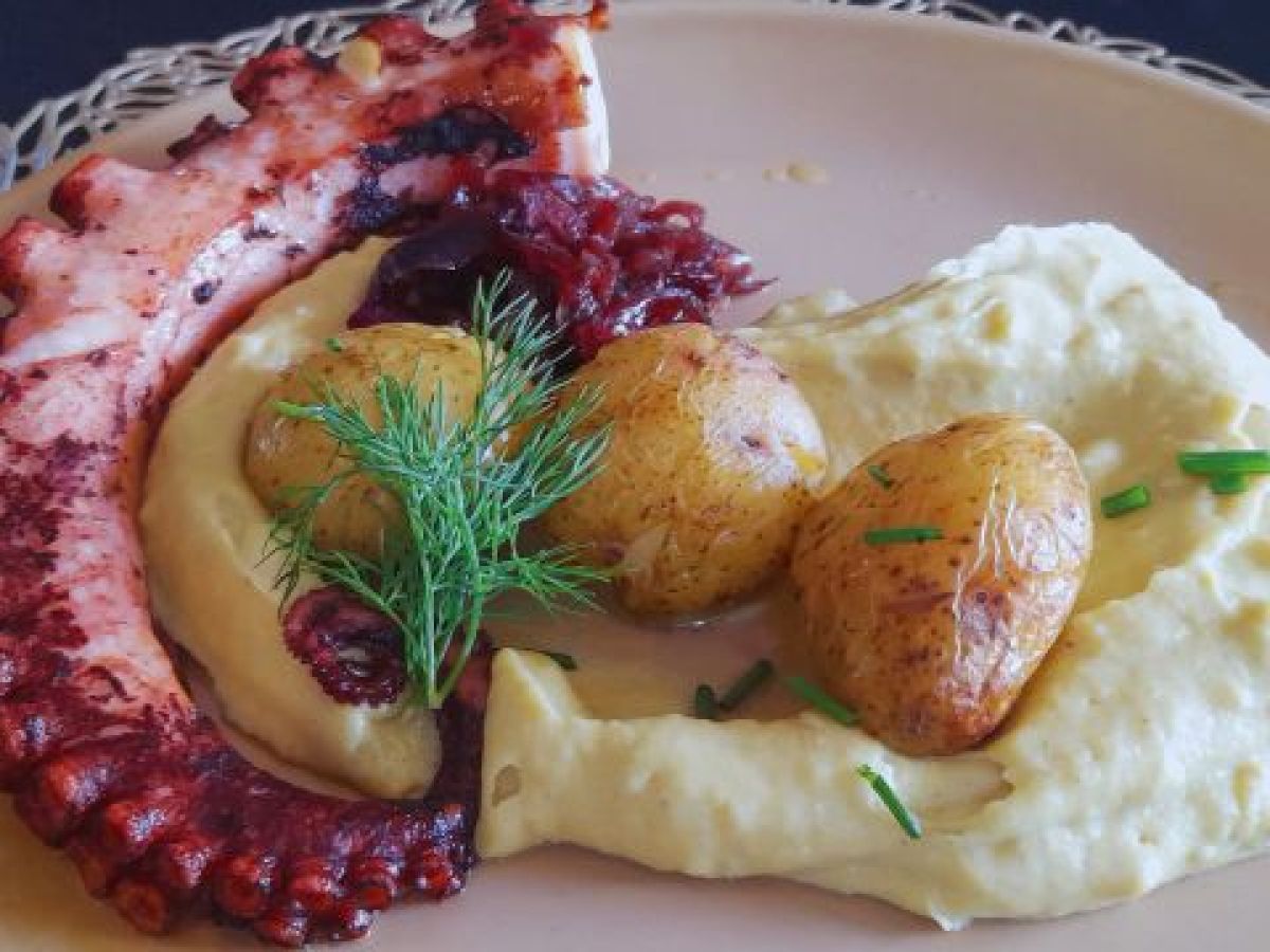 Grilled octopus tentacle with mashed potatoes, roasted potatoes, and garnish.