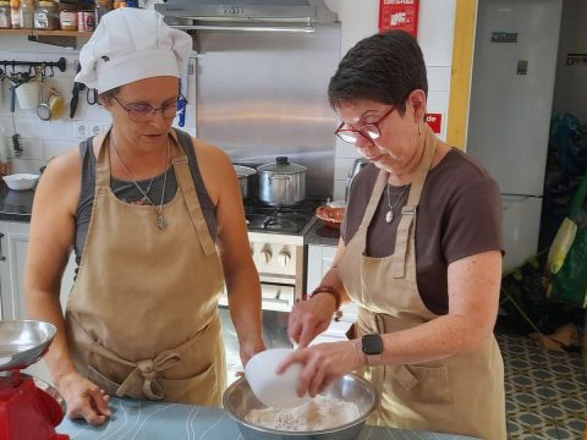 Two women in aprons engage in food preparation in a cozy kitchen, enjoying a cooking class at a picturesque hotel in Portugal